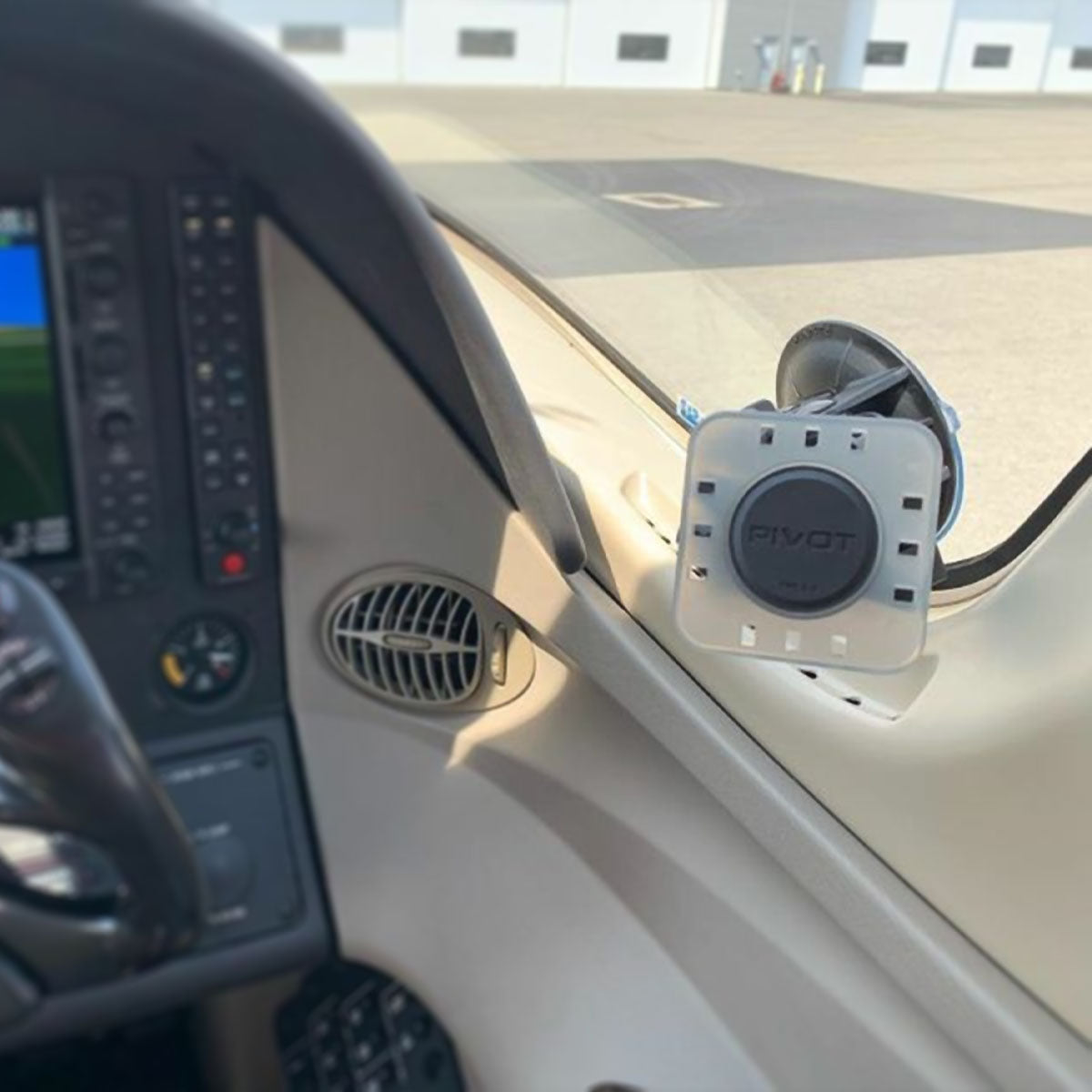 A close-up view of a cockpit interior featuring an attached device mount with the label "PIVOT." The mount is secured to the window and appears ready to hold a device, like a tablet. The instrument panel is partially visible, along with an air vent.