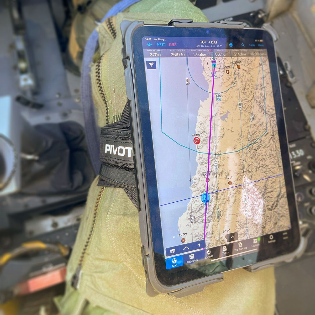 A tablet displaying a navigation map is secured to a person's thigh with a PIVOT strap. The map shows a route over a landscape with various waypoints and geographical features. The person appears to be seated, possibly in an aircraft cockpit.