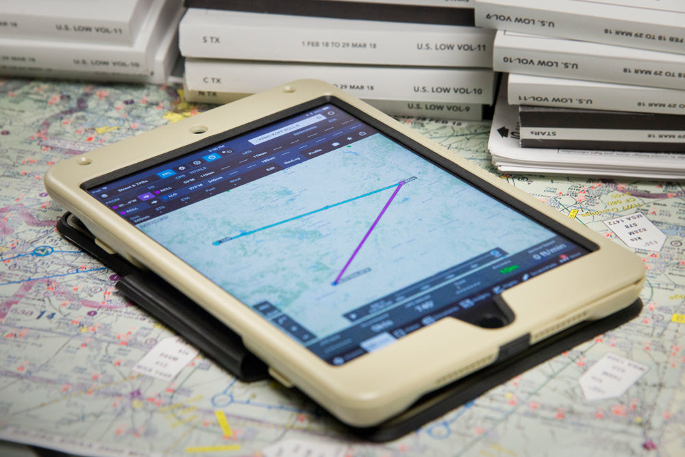 A tablet displaying a flight navigation app with plotted routes on top of aeronautical charts. Nearby, there are stacks of aviation books and documents. The scene suggests flight planning and preparation.