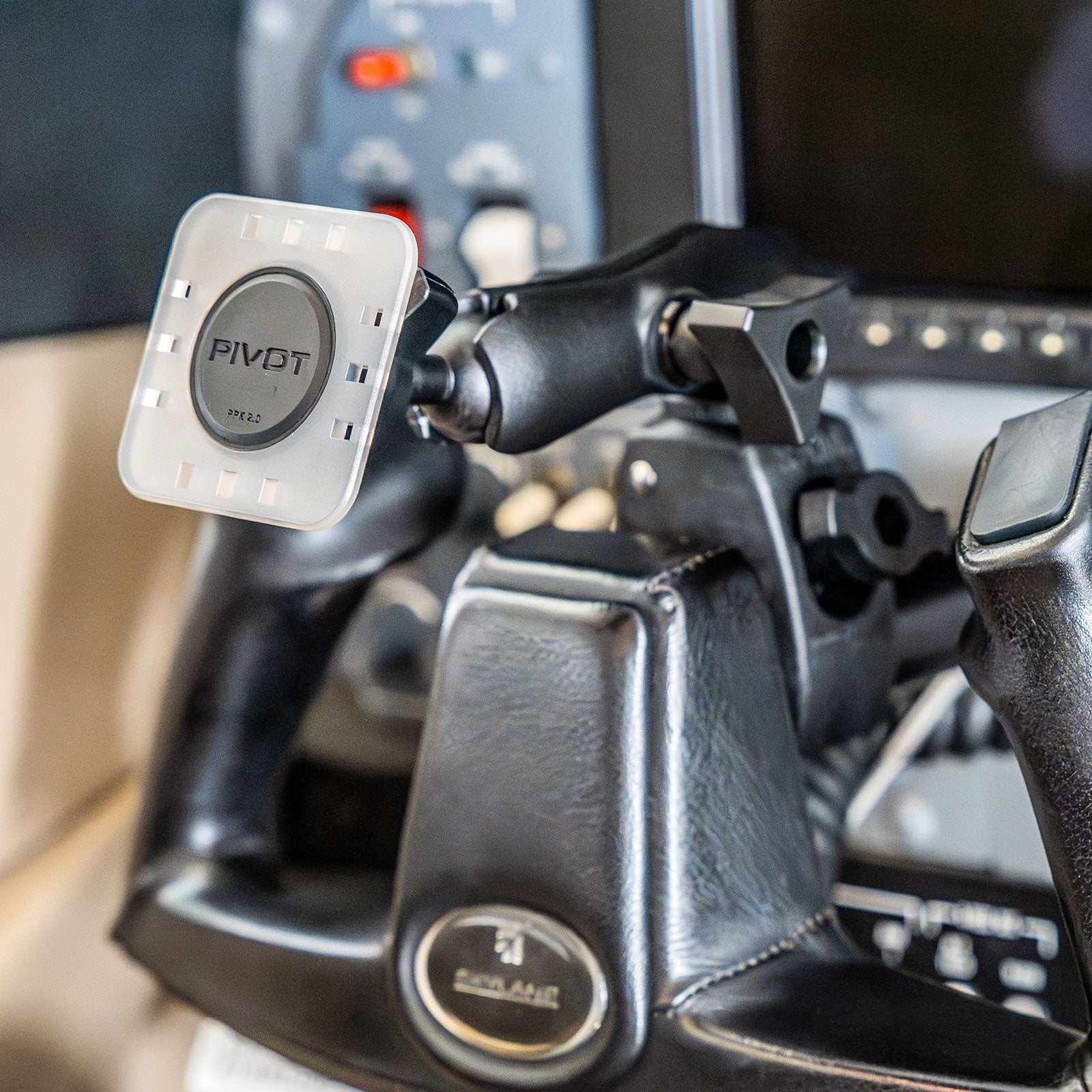 Close-up image of a cockpit showing a PIVOT Claw Mount attached to the control yoke. The mount has a black and white design and is secured in place, highlighting its ergonomics and accessibility for efficient in-flight use. Airplane control panels are visible in the background.