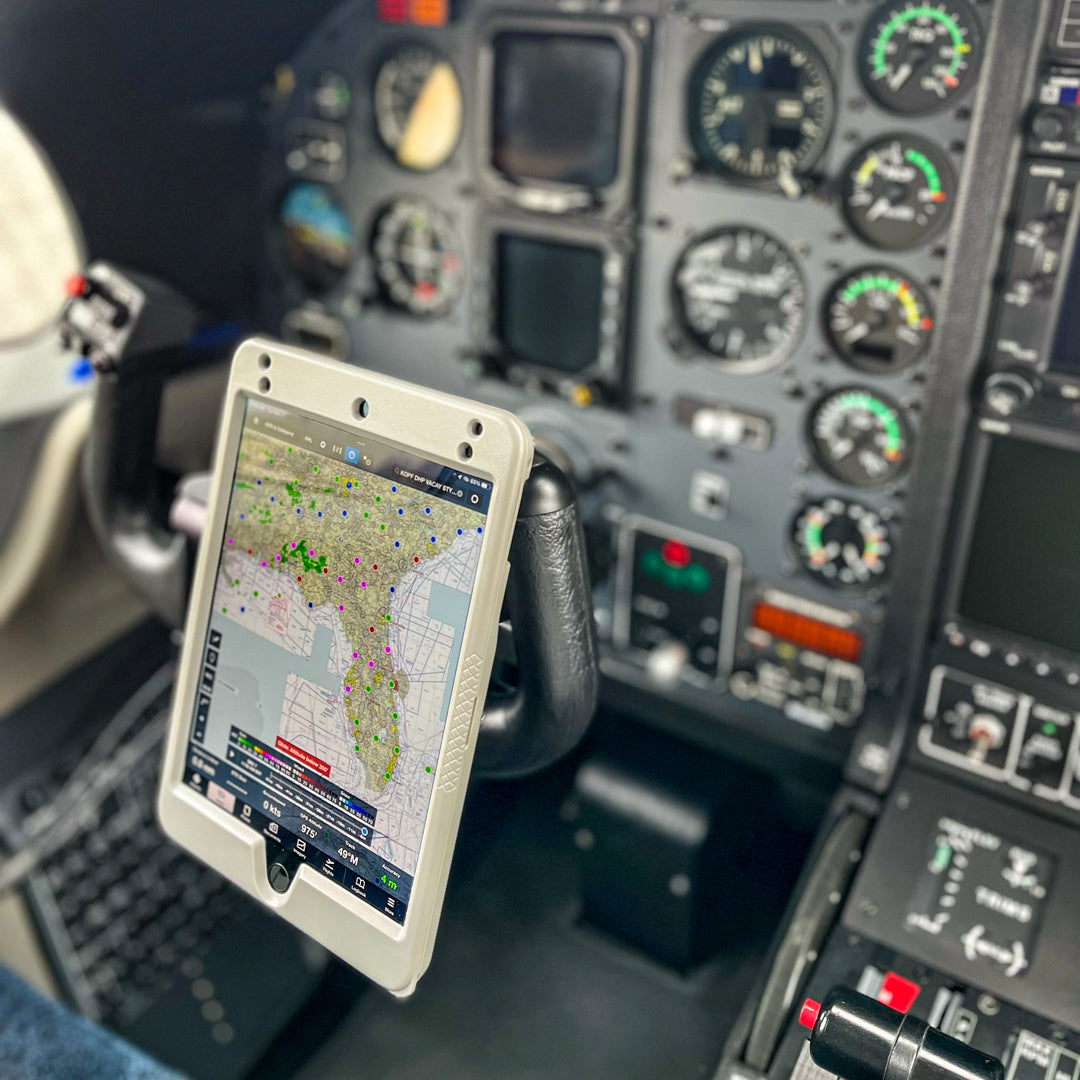 The image depicts the cockpit of an airplane. The main focus is on a tablet mounted on the control yoke using a Claw Mount from PIVOT, displaying a navigational map of Florida. Instrument gauges, switches, and the aircraft's control panel are visible in the background.