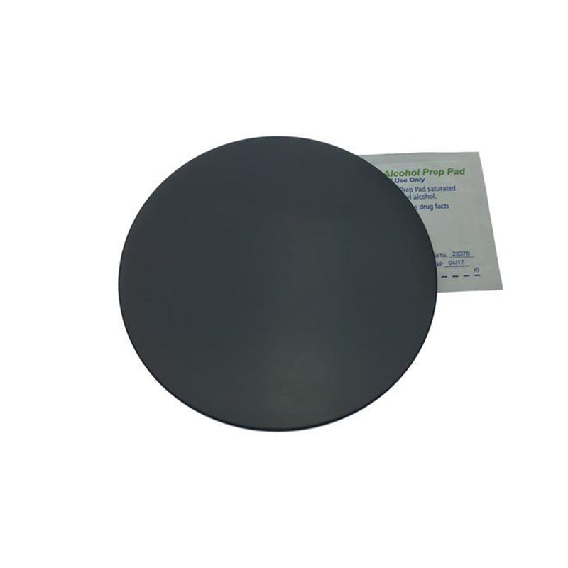 A round black adhesive patch with a separate alcohol prep pad in the background. The PIVOT Suction Cup Mount Sticker Disc by PIVOT is intended for application, while the alcohol prep pad is used for cleaning the area before applying the patch.